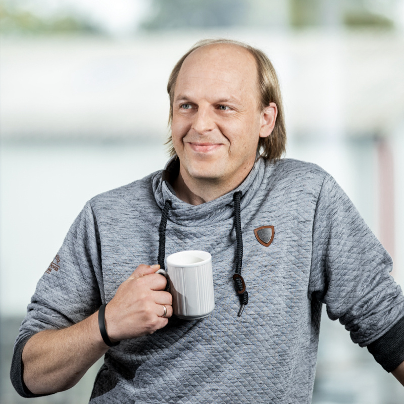 Optitime Mitarbeiter Denis Steigerwald lächelnd mit einem Kaffee